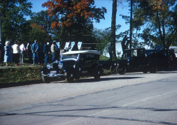 Antique cars parked along the street with actors in the background.