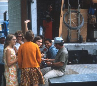 Crew, actors, and others, including Kyle Johnson (Newt Winger) wearing blue denim overalls, mingling in front of production equipment. Johnson appears to be signing autographs for the young ladies in the picture.