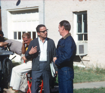 Production crew member conversing with actor George Mitchell (Jake Kiner) dressed in blue denim jacket and jeans, in downtown Ft. Scott, Kansas.