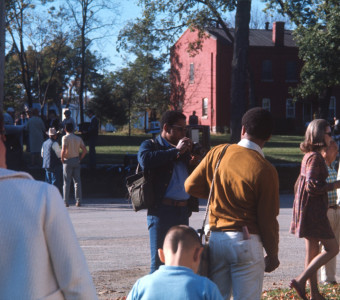 Actor Kyle Johnson (Newt Winger), facing away from the camera, is photographed byGordon Parks' oldest son, Gordon Parks Junior. Various actors and crew members mingle in the street in front of a red brick house.