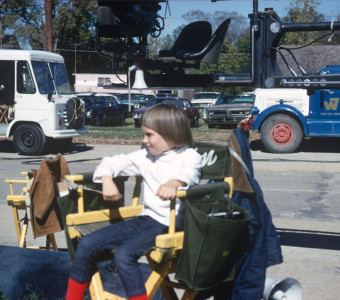 Child sits in Gordon Parks‚Äô director‚Äôs chair amongst film production equipment in downtown Fort Scott, Kansas.