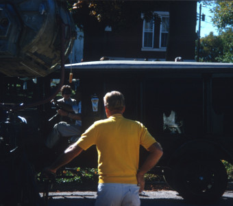 Crewmember in Yellow T-shirt with filming equipment by antique hearse.