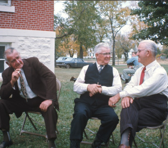Three elderly actors seated outside of courthouse building, dressed for the trial scene. .