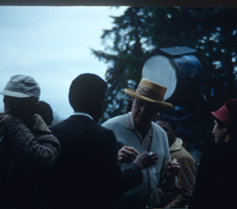 Actor Kyle Johnson (Newt Winger) dressed in a black suit, in conversation with production crew. The photograph was likely taken around the filming of Sarah Winger‚Äôs funeral scene.