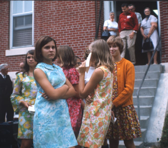 Young women stand in front of the courthouse from the trial scene. The individuals are likely visitors to the set, as they are not present in the trial scene, nor dressed in clothing appropriate for the film‚Äôs time setting.
