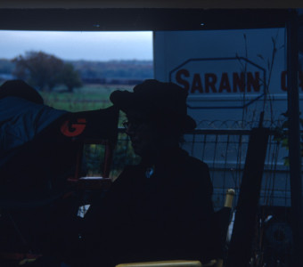 Actress, obscured, seated amongst production equipment.