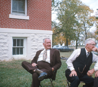Three older actors seated outside of courthouse building from trial scene.