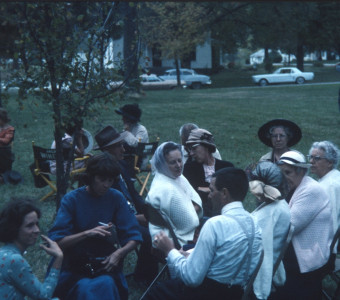 Acting cast members seated in chairs on lawn.