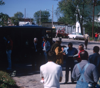 Actors Dana Elcar (Kirky) and Kyle Johnson (Newt Winger) consult book with a crew member with production crew and cast around them. Director Gordon Parks standing behind them in red ascot in front of hearse. Photograph location in downtown Fort Scott, Kansas.