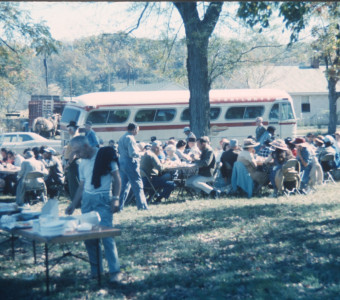 Cast and crew eating a meal outside by production buses.