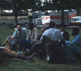 Cast and crew members, including Dana Elcar (Kirky), on ground, Don Dubbins (Harley Davis) with elbow up, and malcolm attebury (Silas Newhall0 in black hat sitting taking a break on a lawn in front of production buses.