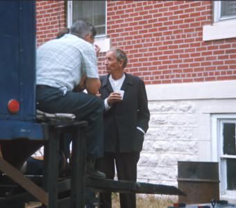 Actor Malcolm Atterbury (Silas Newhall) mingles with crew members at the back of a production truck.
