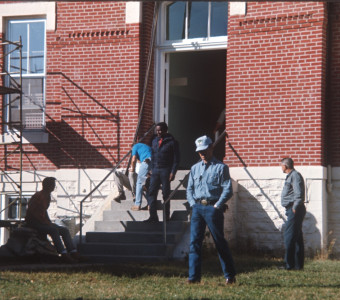 Director Gordon Parks walking down the steps of the courthouse building used for the trial scene with crew members milling about outside.