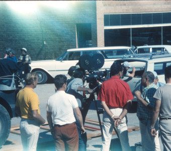 Director Gordon Parks looking through a camera with production crew around him in downtown Fort Scott, Kansas.