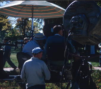 Production crew filming a scene under an umbrella.