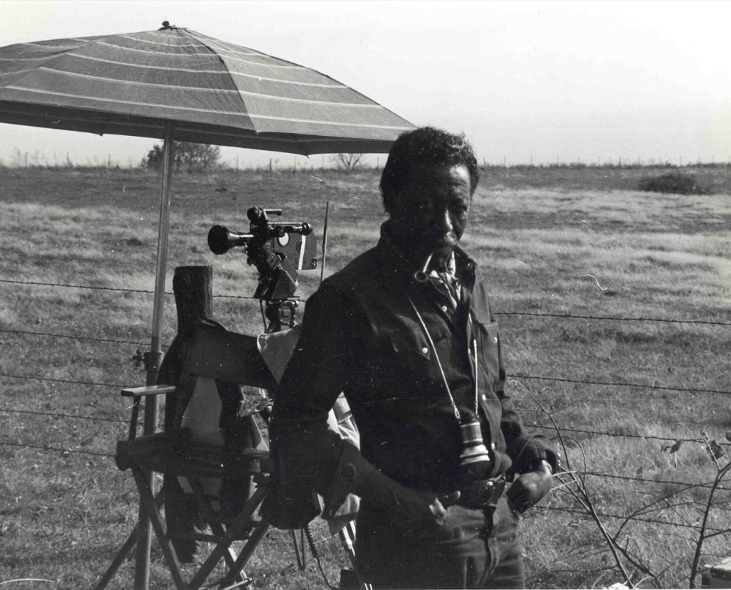 Director Gordon Parks smoking a pipe next to a video camera.