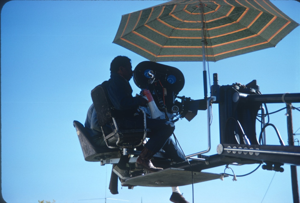Director Gordon Parks filming a scene from above under striped umbrella.