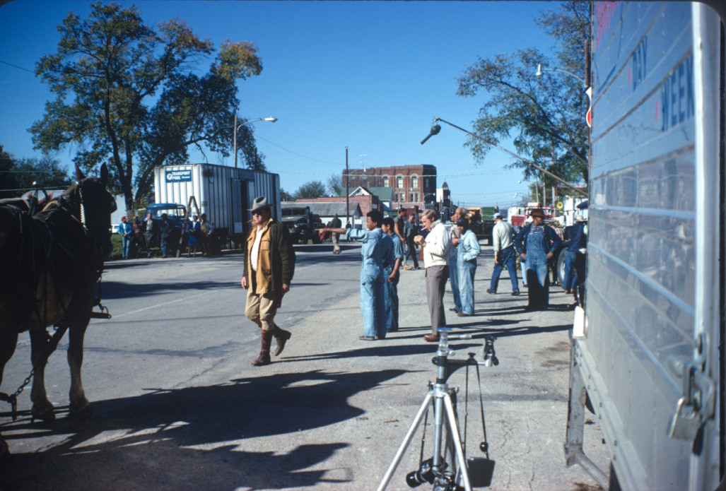 Actors Dana Elcar (Kirky) wearing a tan hat and Kyle Johnson (Newt Winger) in blue overalls, along with other actors and production crew in downtown Fort Scott, Kansas.