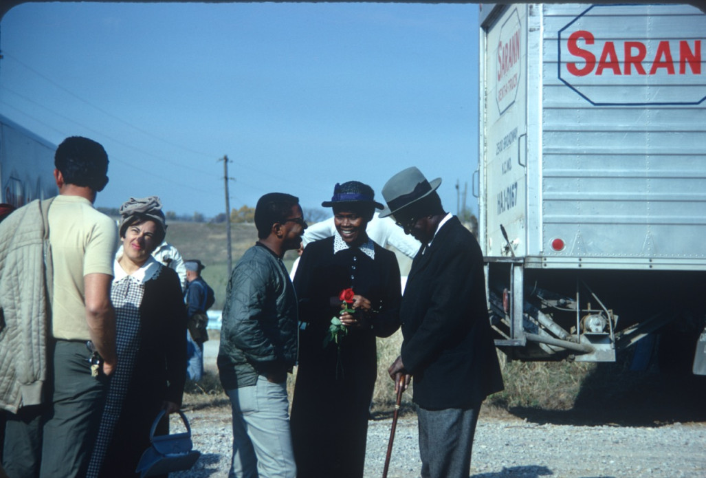 Actresses S. Pearl Sharpe (Prissy) wearing a long black dress, talks with actor Joel Flullen (Uncle Rob) and others. This photograph was likely taken around the filming of Sarah Winger‚Äôs funeral scene.