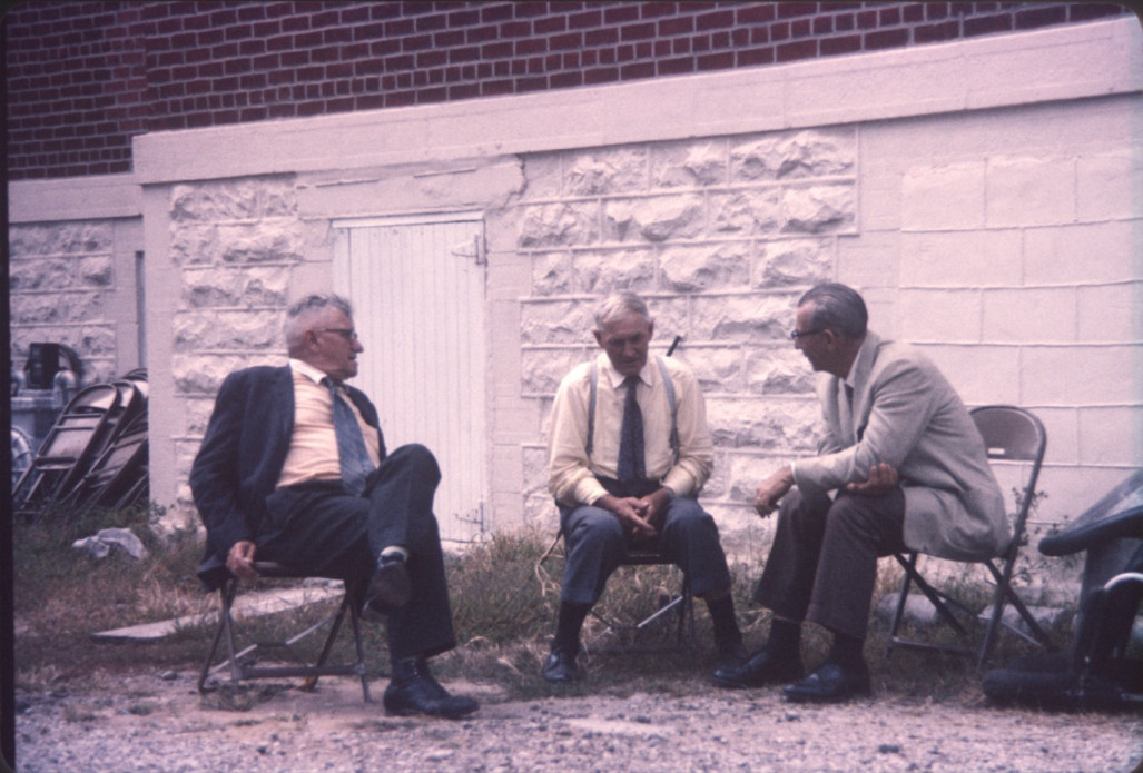 Actor Russell Thorson (Judge Cavanaugh) on left, and two other actors (likely playing jurors) sitting next to the courthouse in the trial scene.