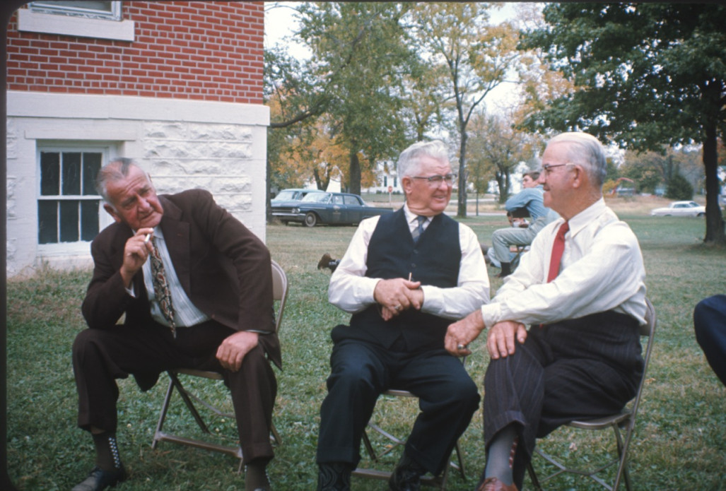 Three elderly actors seated outside of courthouse building, dressed for the trial scene. .