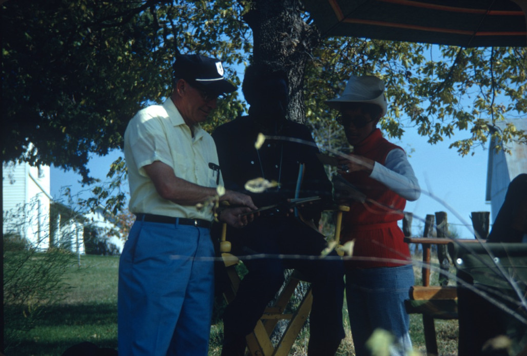 Production crew and Director Gordon Parks (obscured) discussing a document outside of Winger home set.