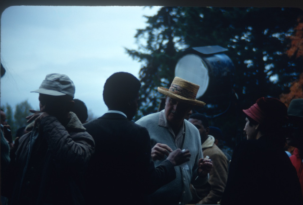 Actor Kyle Johnson (Newt Winger) dressed in a black suit, in conversation with production crew. The photograph was likely taken around the filming of Sarah Winger‚Äôs funeral scene.