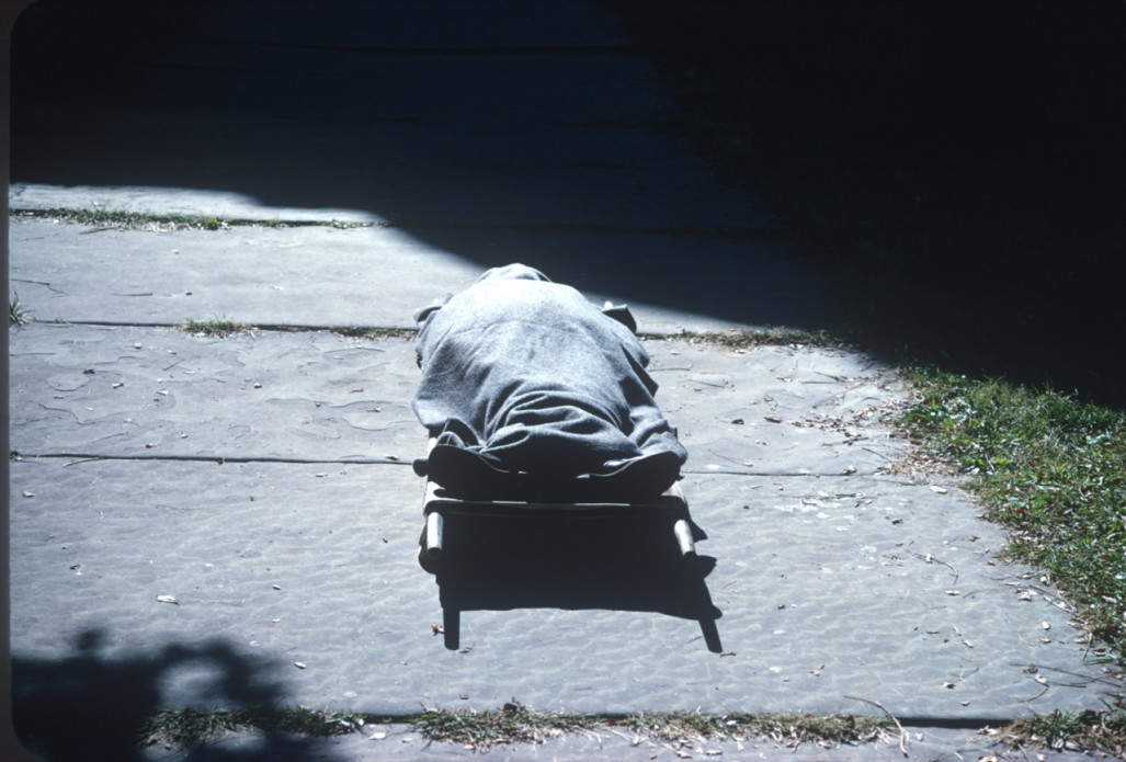 Body on stretcher covered with a blanket. Likely around death scene at creek.