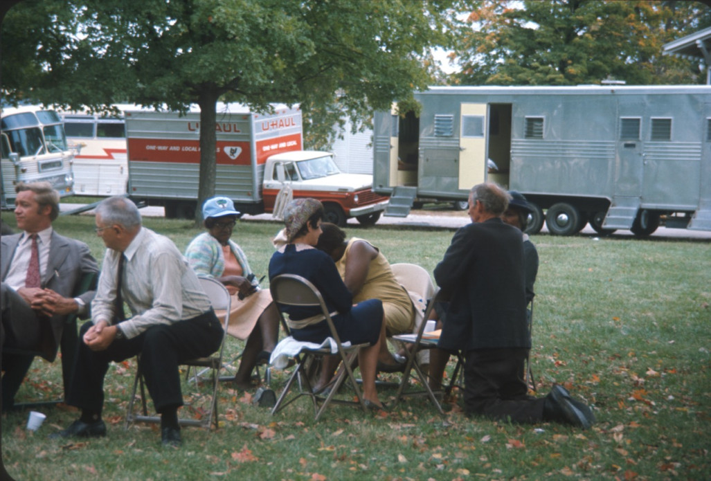 Learning Tree actors sitting in front of trailers Actors, including Estelle Evans (Sarah Winger), obscured by actor Malcolm Attebury (Silas Newhall) and Don Dubbins (Harley Davis), far left, seated in front of production vehicles.