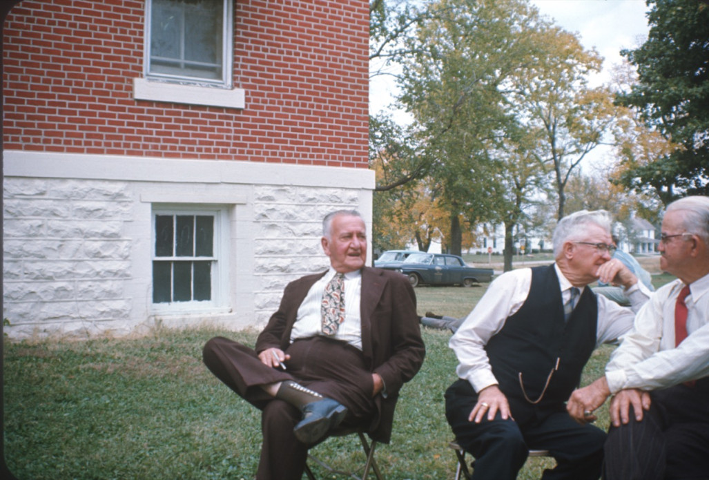 Three older actors seated outside of courthouse building from trial scene.
