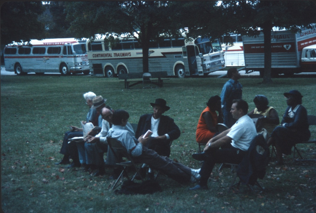 Acting cast, including Estelle Evans (Sarah Winger) on the far right, Stephen Perry (Jappy) standing in blue shirt and overalls, and Malcolm Atterbury (Silas Newhall) in black suit and hat, seated in front of production vehicles.