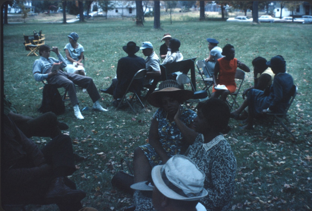 Cast and crew members seated in chairs on lawn; one actor holds The Learning Tree book