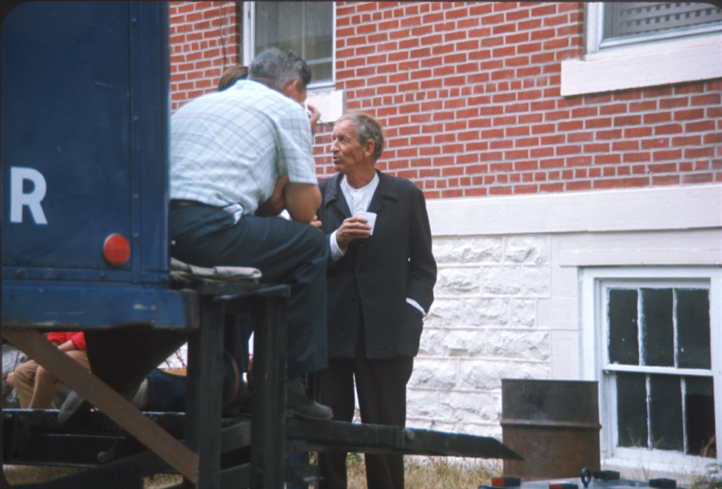 Actor Malcolm Atterbury (Silas Newhall) mingles with crew members at the back of a production truck.