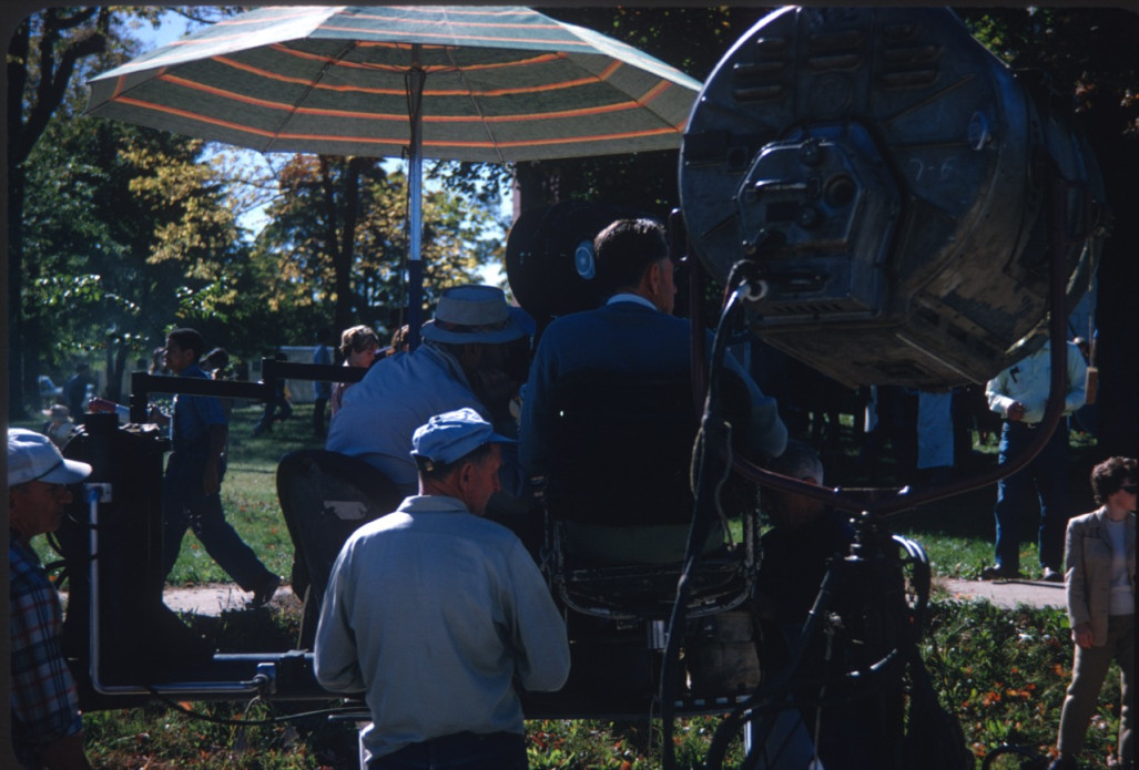 Production crew filming a scene under an umbrella.